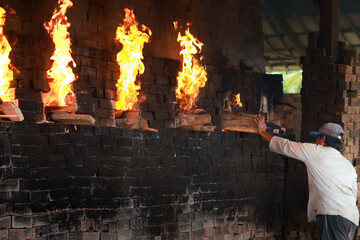 Workers put wood into the stove at traditional red bricks factory, Red brick craftsman use wood for...