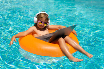 Summer business. Little business man relaxing in the pool with laptop. Kid online working on laptop, swimming in a sunny turquoise water pool.