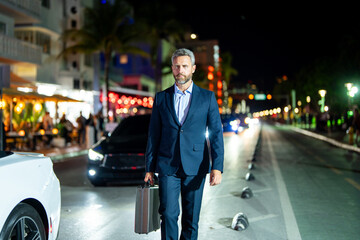 Businessman walking at night city. Rich man in suit walk through city. Businessman near luxury car. Businessman walking near night city lights. Business style. Wealthy businessman in luxury setting.