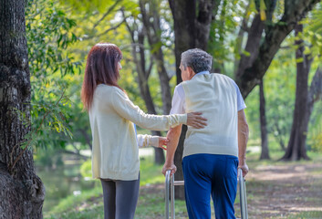 young asian female caregiver help senior man walking with walker in nature park,elderly rehabilitation,health care