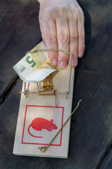 Hand about to take a five euro banknote from a mousetrap