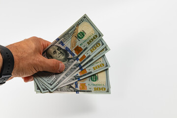 Hand with multiple hundred dollar bills on plain backdrop