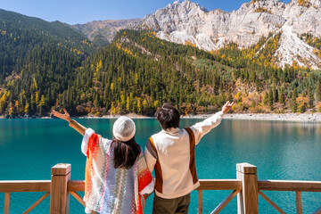 Young couple tourist relaxing and enjoying with beautiful colorful autumn leaves and nature scenic view of Long Lake in Jiuzhaigou national park