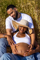 In a beautiful summer setting, a joyful couple expecting their first child enjoys time outdoors, with the husband lovingly embracing his wifes pregnant belly, creating cherished memories