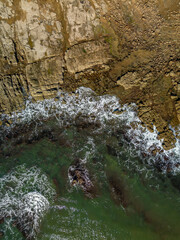 Vertical aerial top down view of ocean waves crashing into rocky shore