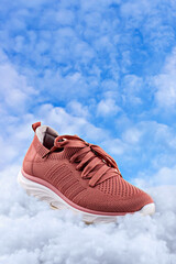 Modern breathable sneaker in muted pink, resting on fluffy cloud-like surface with bright blue sky...
