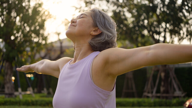 Asia adult aged people middle age mindful happy old woman open arm yoga deep calm stress relief outdoor nature public park sun light self love relax elder aging life asian female mental health care.