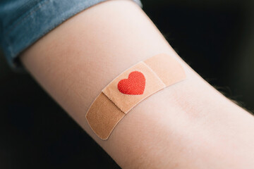 Close-up of a heart-shaped bandage on a human arm
