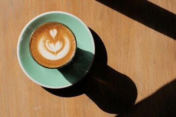 Latte art in a cup on a wooden surface with sunlight and shadow.