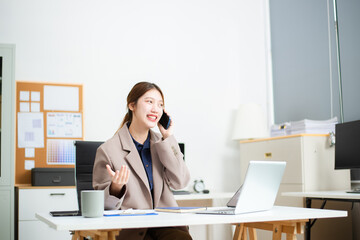 Confident businesswoman multitasking at desk with phone, laptop, and documents in a bright office.
