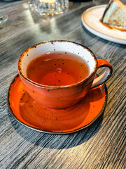 A comforting and inviting scene with orange ceramic mug with hot tea rests on a wooden table. Made on smartphone.