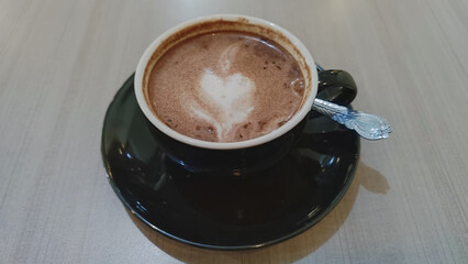 Top view of a cup of hot chocolate with heart-shaped latte art on a wooden table. Cozy and warm beverage in a black ceramic cup and saucer.