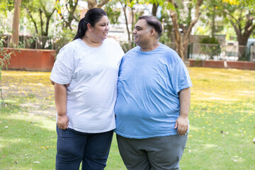 Obraz premium Happy Overweight indian couple looking at each together in summer park. Plus size man and woman looking camera. Fat people india. Obesity concept.