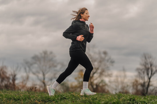 Young sportswoman running in a park on cloudy day - Powered by Adobe