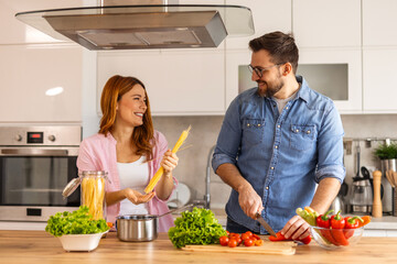 Smiling young couple cooking food in the kitchen together in the kitchen,having a great time together. Man and woman laughing