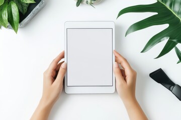 Hands holding white tablet mockup style isolated on white background. Person is holding a tablet with a black screen. The tablet is on a white background with green leaves.