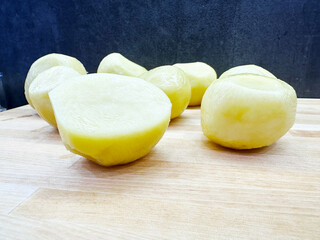 Peeled potatoes on wooden surface with dark background