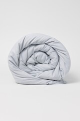 Studio photo of a light grey comforter rolled tightly into a spiral, placed on a clean white background. The fabric is soft, smooth, and slightly matte, with gentle folds 