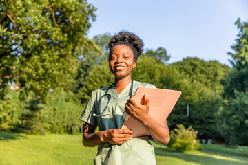 Smiling dark-skinned woman in a lab coat on a greenery background