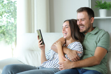 Fototapeta premium Happy couple enjoying watching media on mobile phone