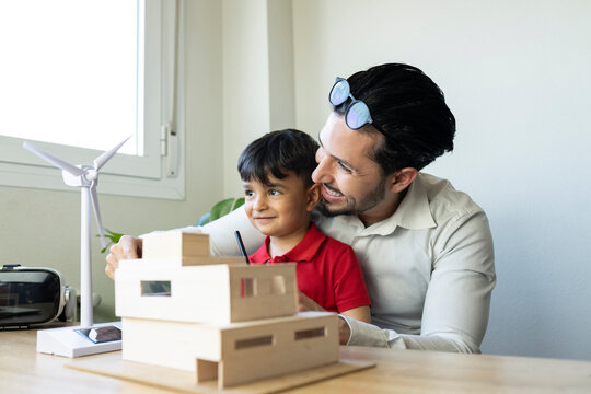 Male architect and son smiling while looking at wind turbine model at home