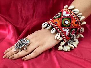 Hand wearing a vibrant embroidered Navratri kada bangle adorned with Kodi shells and oxidized ring,...