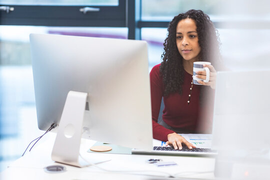 Businesswoman holding mug and using computer at desk in office