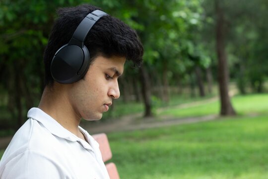 Young man with headphones in a lush green park, listening intently. - Powered by Adobe