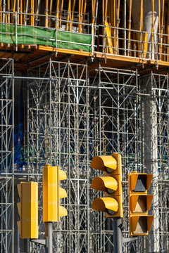 Urban construction site with yellow scaffolding, traffic lights, industrial structures, geometric elements, city development scene.