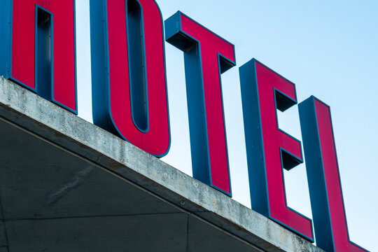 Fototapeta Red hotel sign, modern typography, geometric shapes, minimalist architecture, blue sky, bold contrast in urban scene.