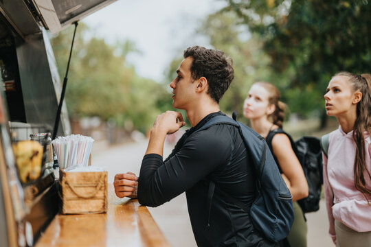 Friends gather to order refreshments at a food truck in a park, showcasing social interaction, outdoor activities, and a casual urban lifestyle.
