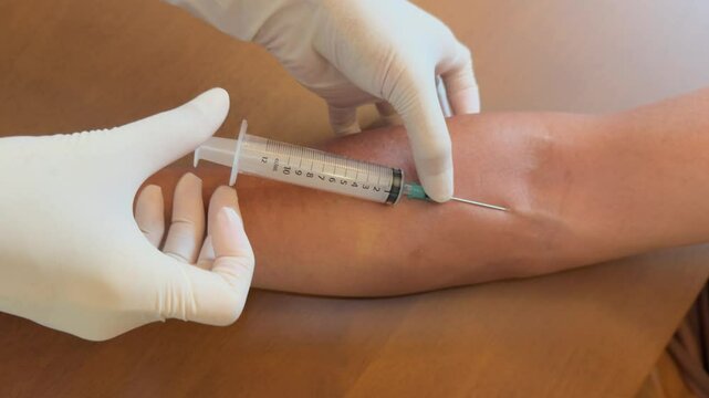Handheld top view of a medical professional inserting a needle into a patient's arm vein and drawing blood into a collection tube.