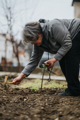 An elderly woman actively engaged in gardening, holding tools and tending to plants in a natural outdoor setting, symbolizing care, vitality, and the enjoyment of nature's beauty.