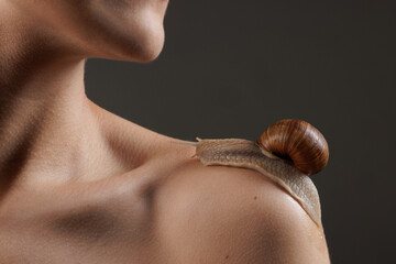Close-up of a snail crawling on a woman's bare shoulder during a cosmetic skincare treatment, highlighting the natural, hydrating, and rejuvenating benefits of snail therapy. © st.kolesnikov