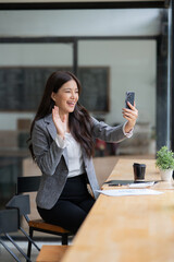 Asian businesswoman using laptop, smartphone, talking about work at bar, coffee shop
