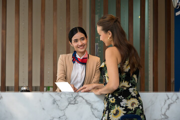 Hotel receptionist with friendly smile assists female guest at marble front desk and engaging in...