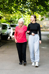 Fototapeta premium Supportive stroll through a tranquil neighborhood with a young woman and her elderly companion, enjoying a sunny afternoon filled with laughter and connection