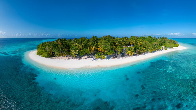 A drone view of an island with white sand in the middle of the ocean. Turquoise water, coral reef. There are palm trees all around. Maldives