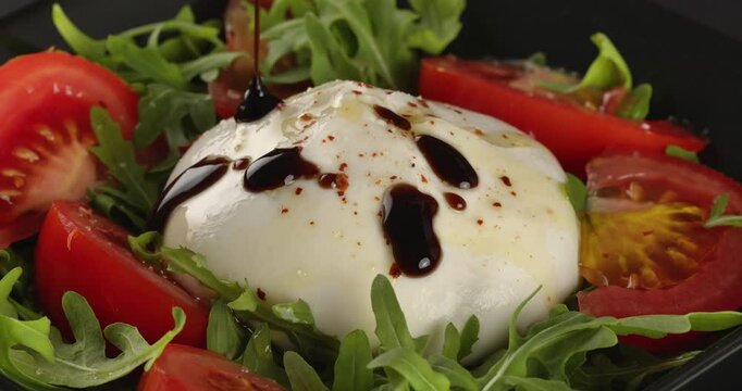 Burrata cheese with tomatoes and arugula drizzled with balsamic vinegar. Close-up footage on the rotating table.