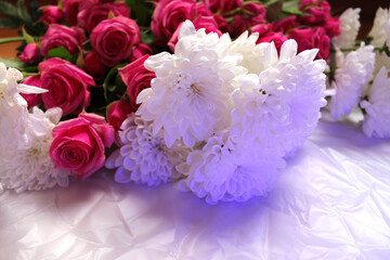 A rich bouquet of vibrant pink roses and white chrysanthemums laid on a pearlescent background, lit with soft daylight.