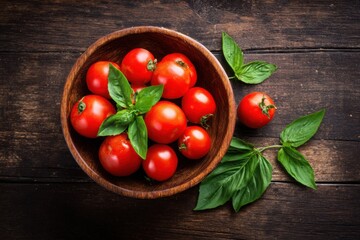 Top view of a wooden bowl filled with cherry tomatoes and fresh basil leaves on a dark rustic kitchen table setting.