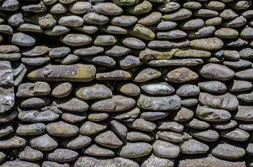 Close-up of weathered stone wall exhibiting varied shapes and textures. Sunlight highlights natural...