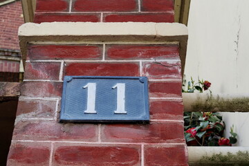 Numéro 11. Plaque de numéro de rue sur façade de brique rouge.