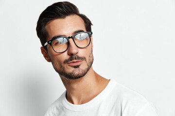 Stylish handsome young man in glasses poses confidently while looking away from the camera,...
