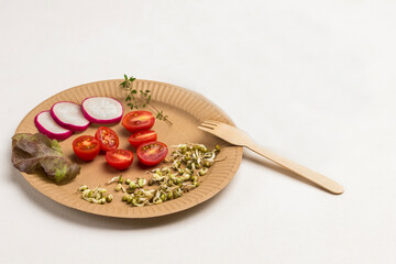 Germinated mung bean sprouts, halved tomato and slices of radish on cardboard disposable plate. Fork on plate.