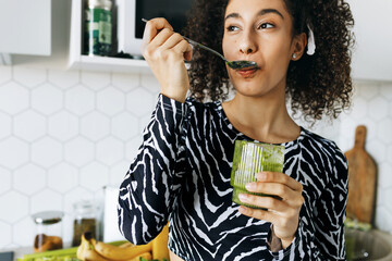 Indoor portrait of young healthy black slim girl leaning against kitchen counter full of fruits,...