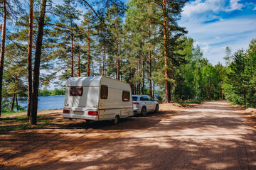 Caravan RV parked on the beach under a trees facing blue sea, lake or river. Family traveling with motorhome. Travelers on an active family vacation.