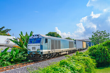 Freight train wagons container locomotive travels along the railway drives among the trees in a tropical town © aapsky