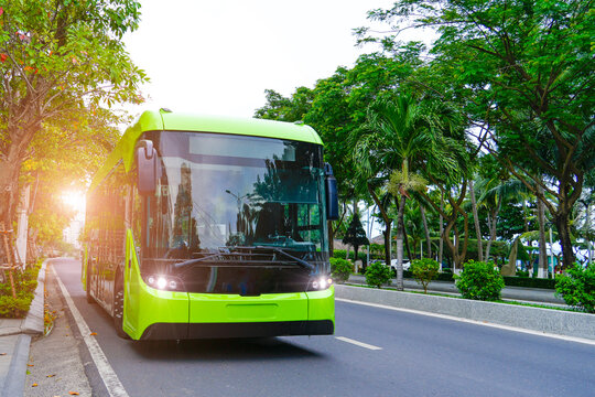 Electric bus with headlights on drive down the street among trees and stop route