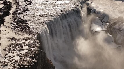 Dettifoss waterfall thundering through snowy Icelandic terrain, epic drone view, Europe's most powerful falls in winter light. - Powered by Adobe
